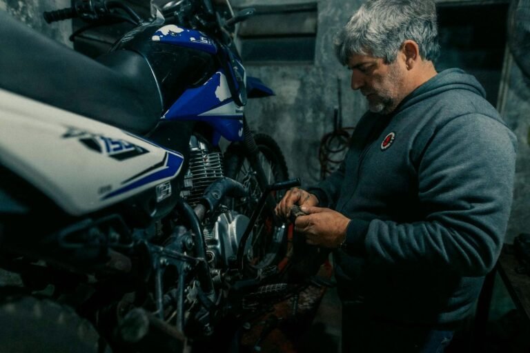 An adult man repairs a motorcycle in a dimly lit garage, showcasing mechanical expertise.