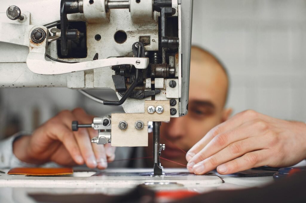 Unrecognizable artisan using sewing machine for sewing on leather fabric piece while creating handmade details in workshop