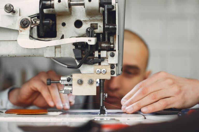 Unrecognizable artisan using sewing machine for sewing on leather fabric piece while creating handmade details in workshop
