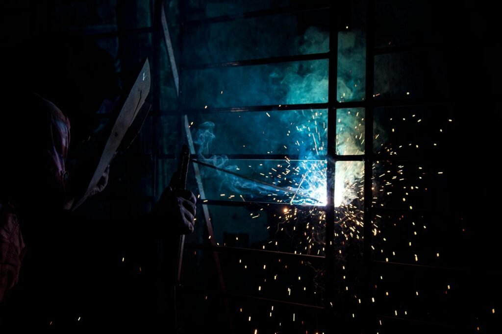 A welder works in a dimly lit workshop, sparks flying as metal is welded.