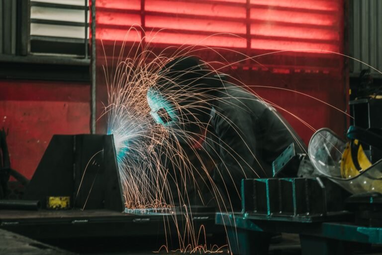 A welder skillfully creates sparks while working in an industrial workshop, wearing protective gear.