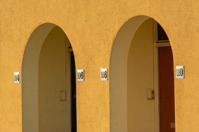 Close-up of yellow arched walls with apartment numbers in an urban setting.