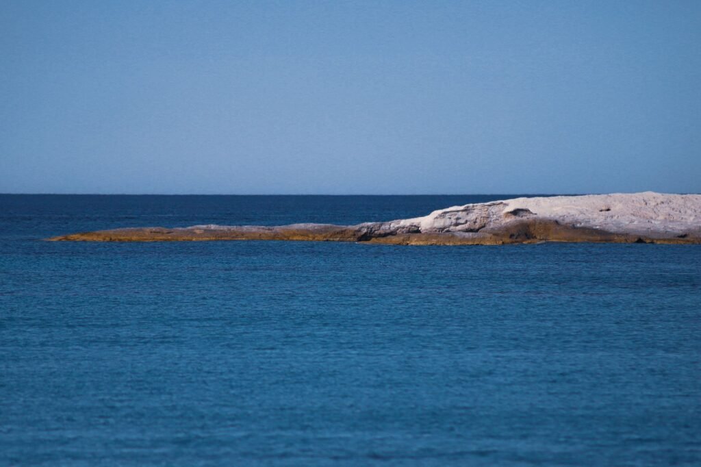 Serene view of a rocky island in a vast blue ocean under a clear sky, perfect for tranquil escapes.