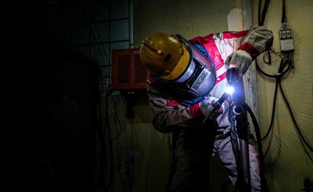 A welder wearing protective gear works with a torch indoors, highlighting industrial labor.