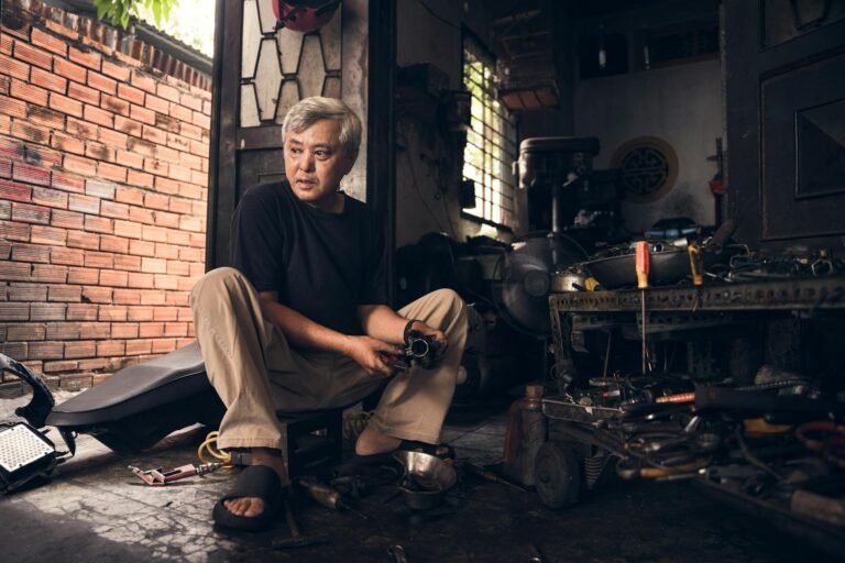 Elderly artisan in Ho Chi Minh City garage working with tools and machinery.