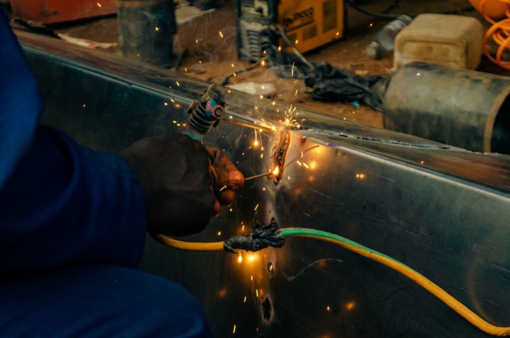 Close-up of a welder working on metal with sparks flying in an indoor workshop setting.